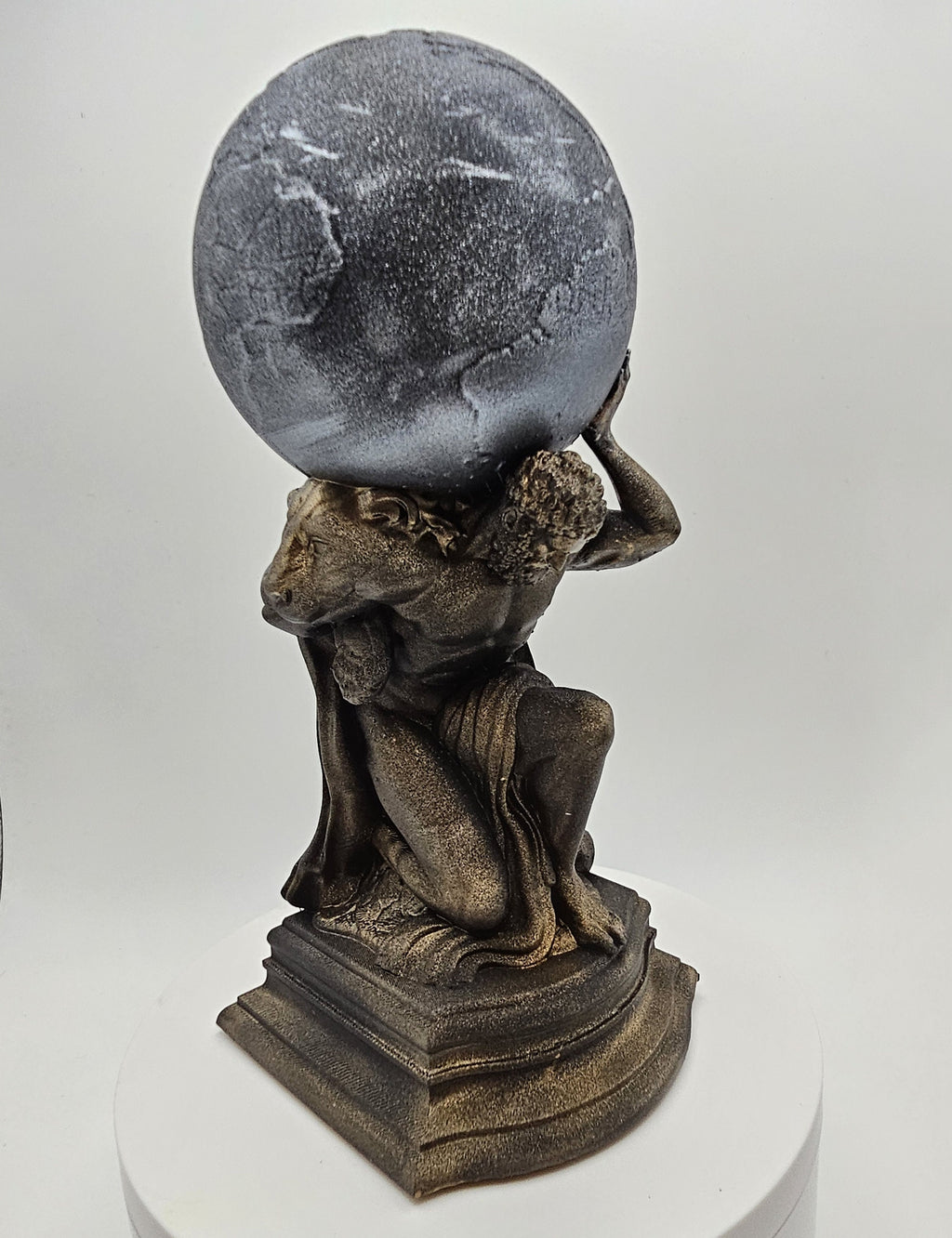 A detailed figurine of Atlas carrying the globe on his shoulders, showcasing a classic mythological design with intricate bronze and silver tones, displayed on a pedestal base.