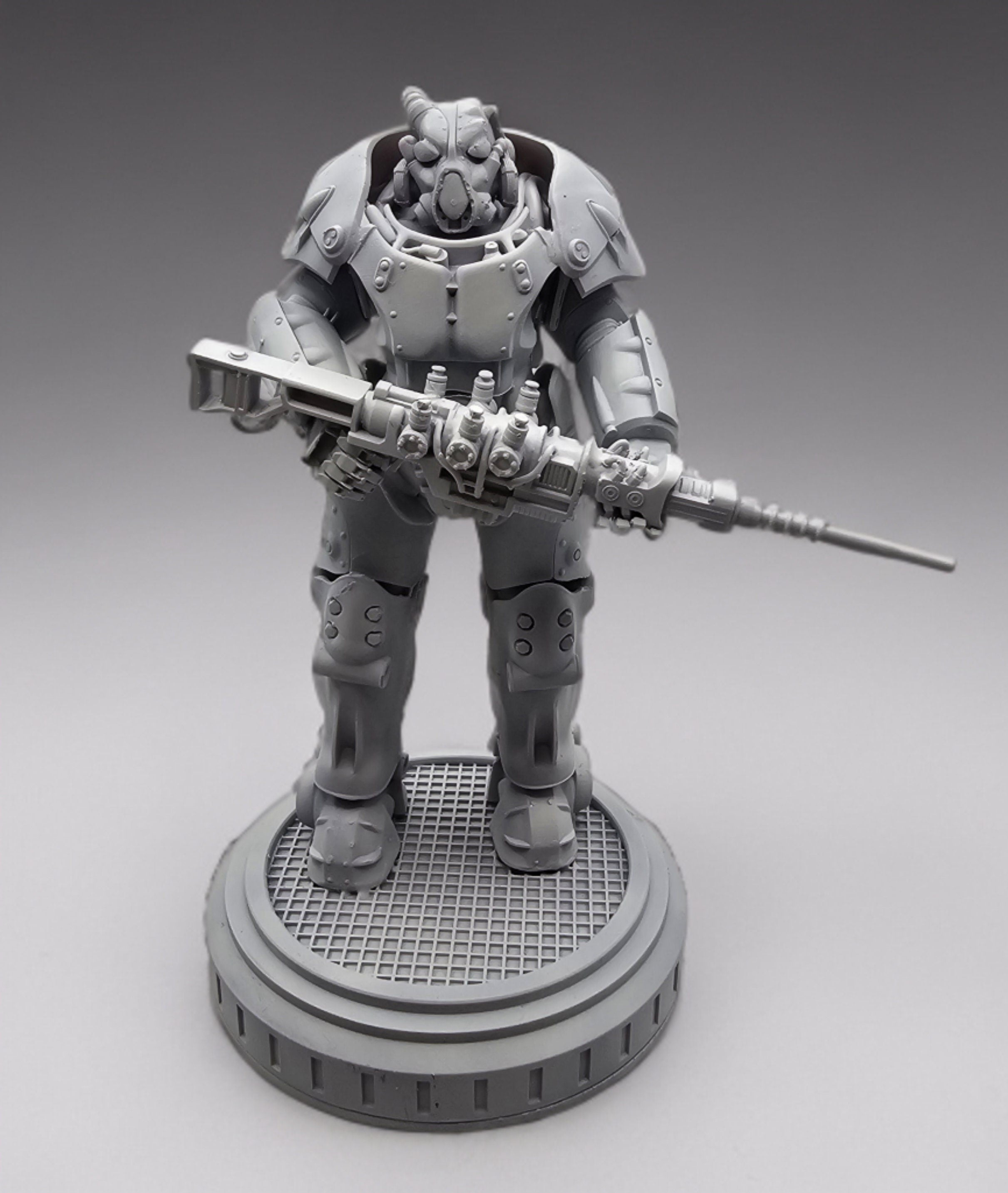 A gray plastic figurine of a robot wearing a helmet and holding a gun. The robot is standing on a round base with a textured surface.