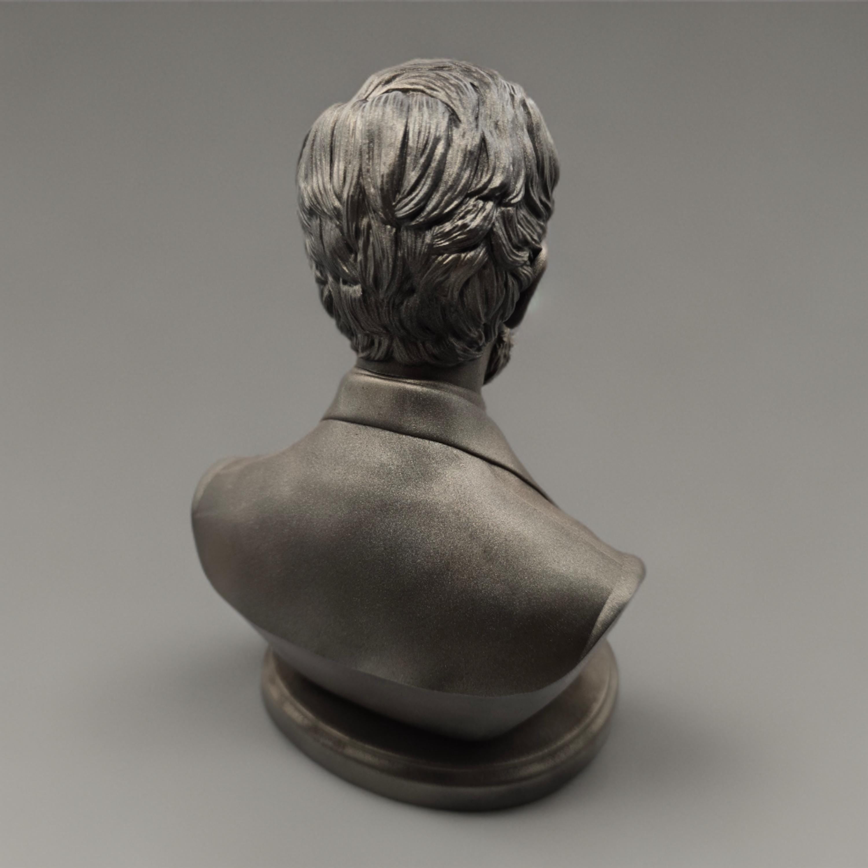 Silver-colored bust statuette of Abraham Lincoln, showcasing detailed facial features, a neatly trimmed beard, and formal attire with a bow tie, mounted on a rectangular base.