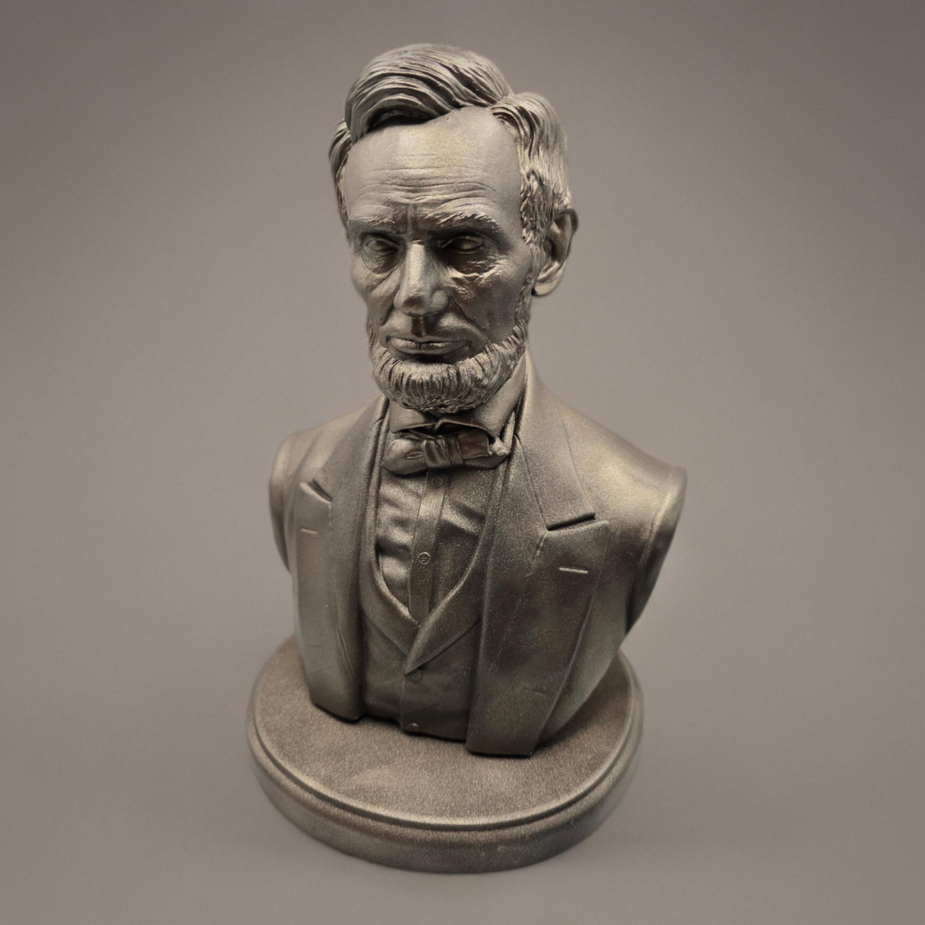 Silver-colored bust statuette of Abraham Lincoln, showcasing detailed facial features, a neatly trimmed beard, and formal attire with a bow tie, mounted on a rectangular base.