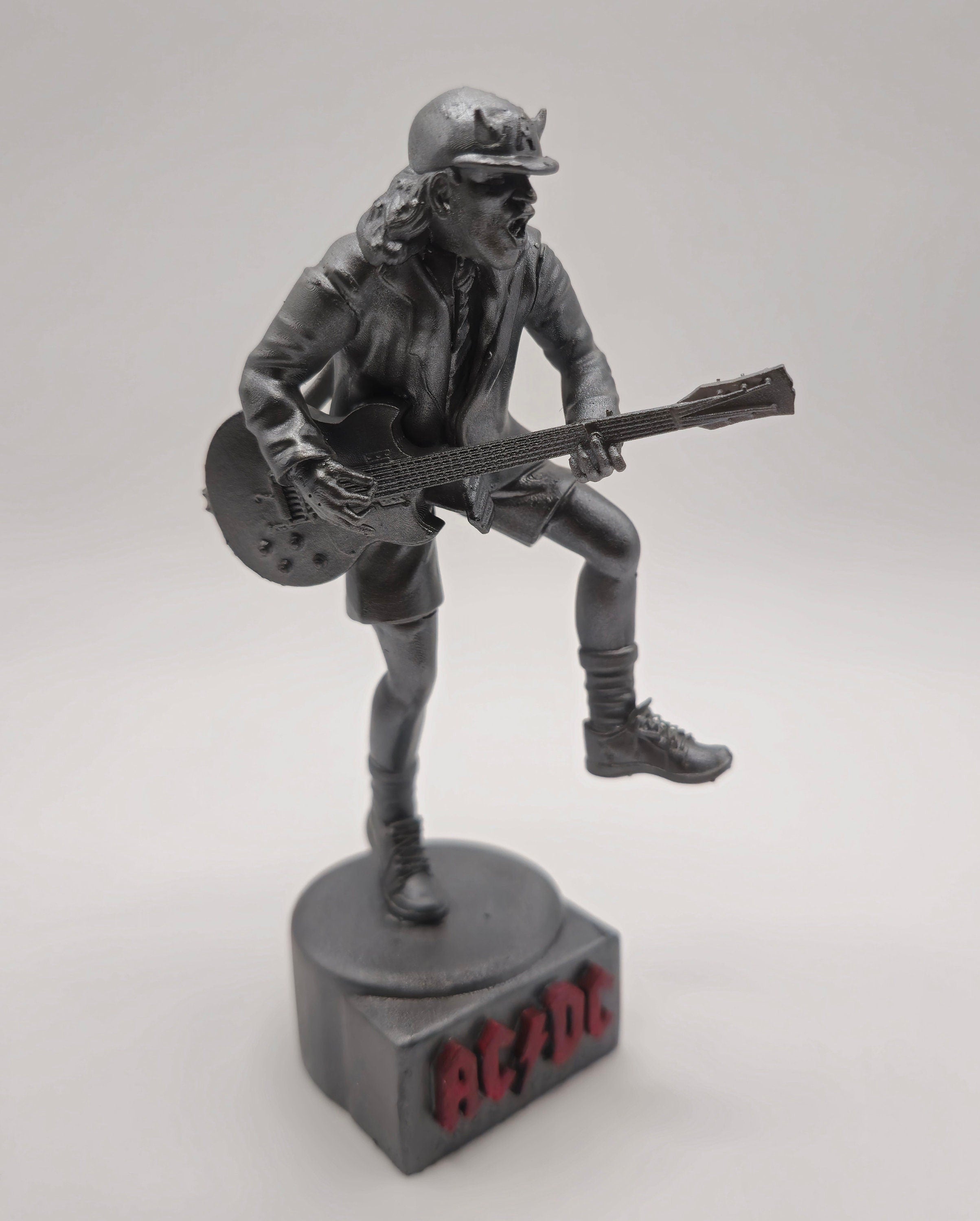 Statue of Angus Young from AC DC, depicted in a dynamic pose with his iconic guitar and schoolboy uniform, standing on a base engraved with the band's logo.