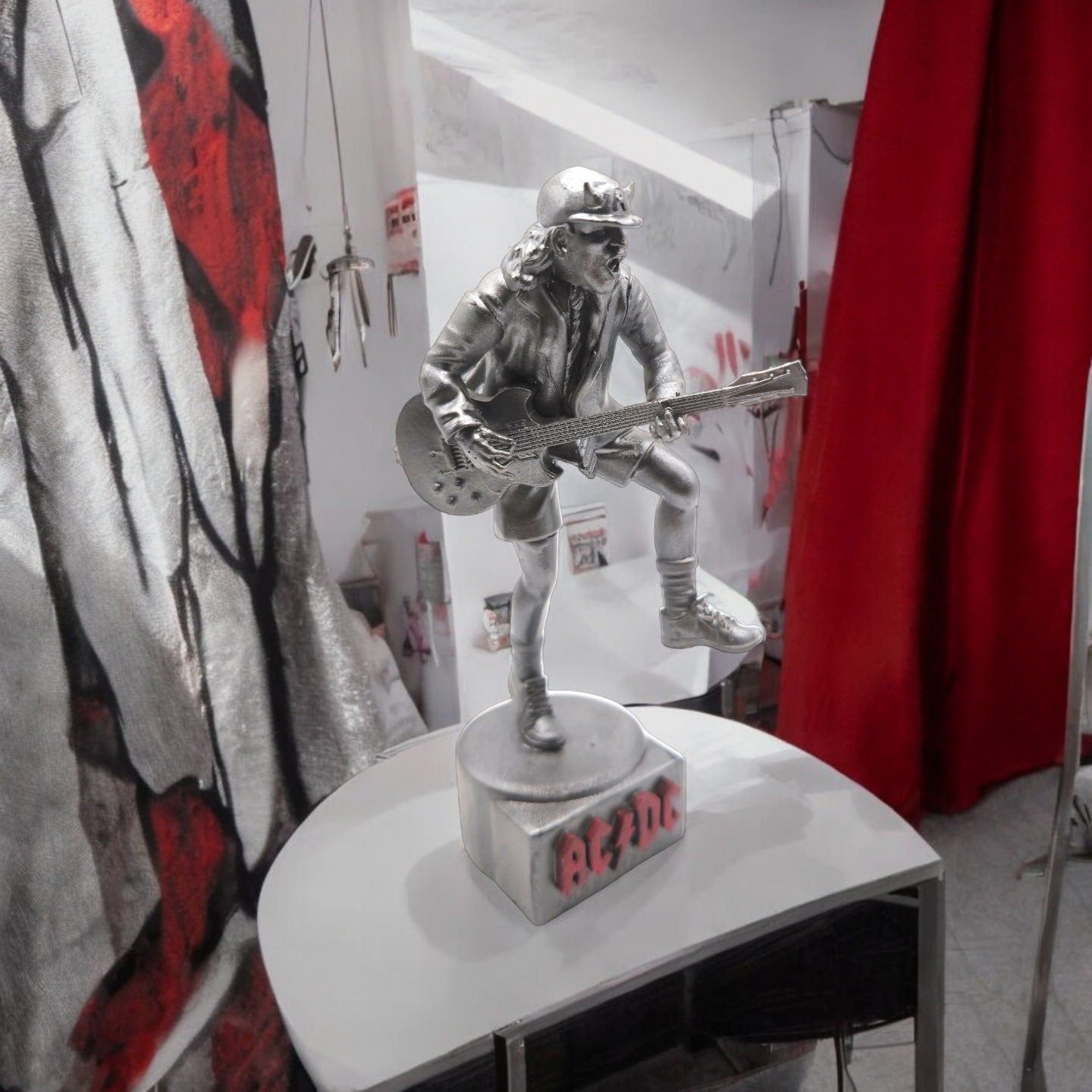 Statue of Angus Young from AC DC, depicted in a dynamic pose with his iconic guitar and schoolboy uniform, standing on a base engraved with the band&#39;s logo.