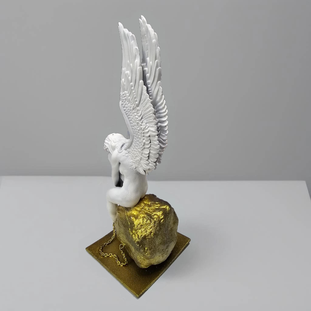 Statue of a chained angel seated on a textured pedestal, with detailed wings and a contemplative pose.