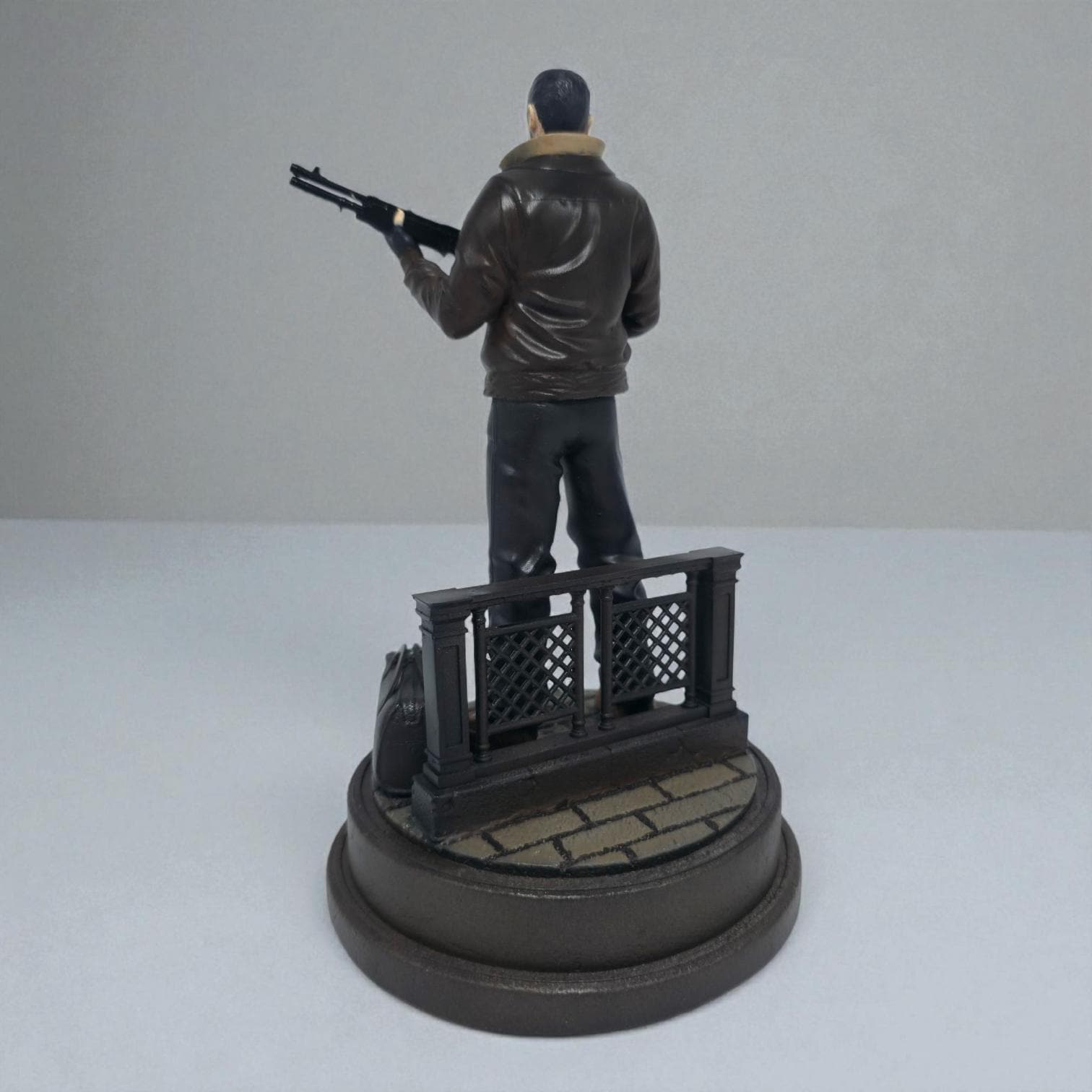 Highly detailed 3D-printed figurine of a rugged man holding a shotgun, standing confidently on a circular base marked with “Liberty City,” accompanied by a duffel bag and fence detail, perfect for collectors.