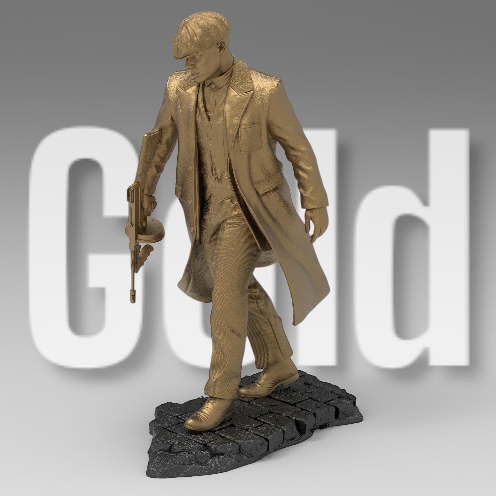 A bronze-colored figurine depicts a man in a long coat and newsboy cap, holding a submachine gun. He stands on a textured, dark gray base, styled as a cobblestone street. The figurine is detailed, capturing the texture of the fabric and the weapon.  The overall style suggests a gangster or 1920s era figure.